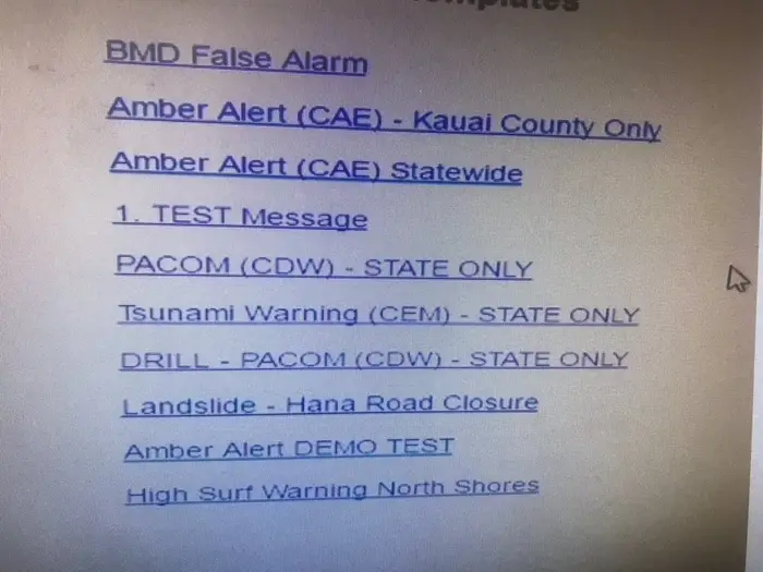 A mockup of the alert screen, blue link text on a white background. It lists the following options: BMD False Alarm, Amber Alert (CAE) - Kauai County Only, Amber Alert (CAE) Statewide, 1. TEST Message, PACOM (CDW) - STATE ONLY, Tsunami Warning (CEM) - STATE ONLY, DRILL - PACOM (CDW) - STATE ONLY, Landslide - Hana Road Closure, Amber Alert DEMO TEST, High Surf Warning North Shores